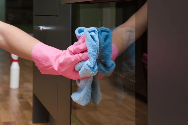 Personne en gants roses de protection nettoyant une surface vitrée avec un chiffon microfibre bleu dans un environnement intérieur moderne