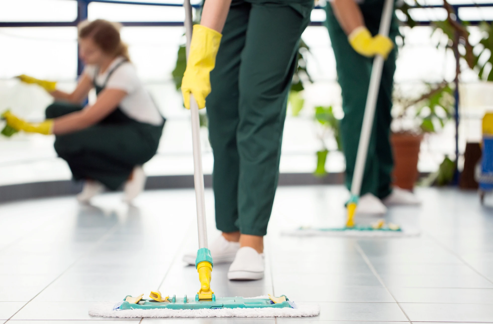 Personnel de nettoyage professionnel en uniformes verts avec gants jaunes effectuant l'entretien d'un hall d'accueil moderne