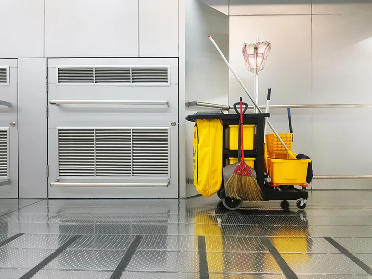 Couloir intérieur commercial avec chariot de ménage professionnel jaune et noir équipé de seau à essoreuse, balai à franges, sac à déchets et produits d'entretien