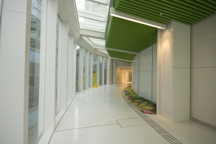 Couloir moderne d'immeuble de bureaux avec sols carrelés blancs brillants, murs blancs, larges baies vitrées sur la gauche donnant sur l'extérieur