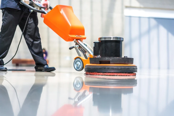 Intérieur d'un bâtiment commercial moderne avec travailleur utilisant une monobrosse professionnelle pour nettoyer un sol carrelé brillant