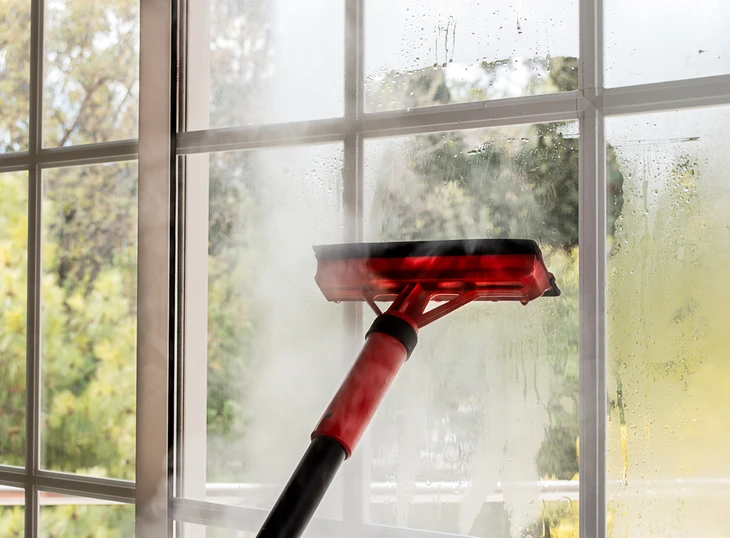 Nettoyage de vitres à l'intérieur d'un bâtiment, raclette professionnelle rouge et noire en action sur une fenêtre à carreaux