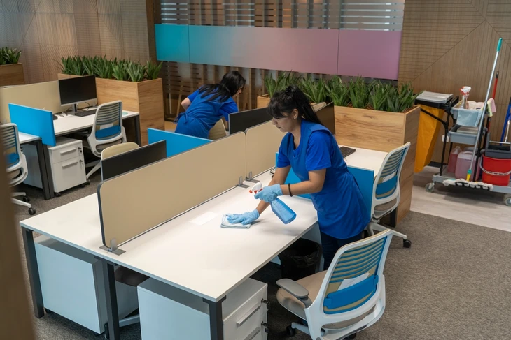 Bureau moderne avec personnel de nettoyage professionnel en uniforme bleu désinfectant postes de travail