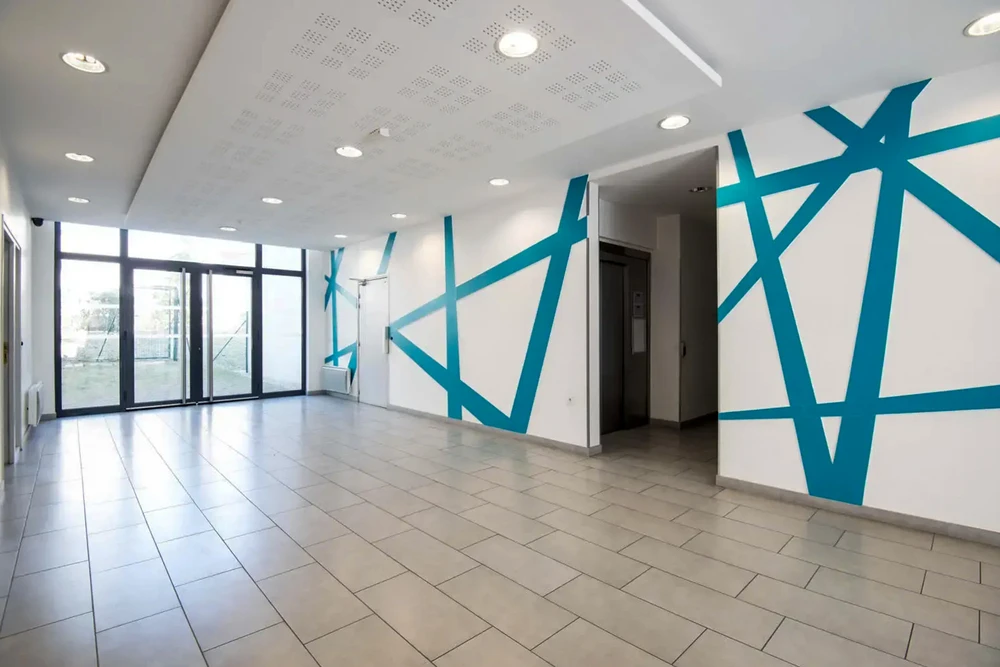 Hall d'entrée moderne et vide, murs blancs ornés d'un décor graphique abstrait en bandes turquoise/cyan formant des polygones