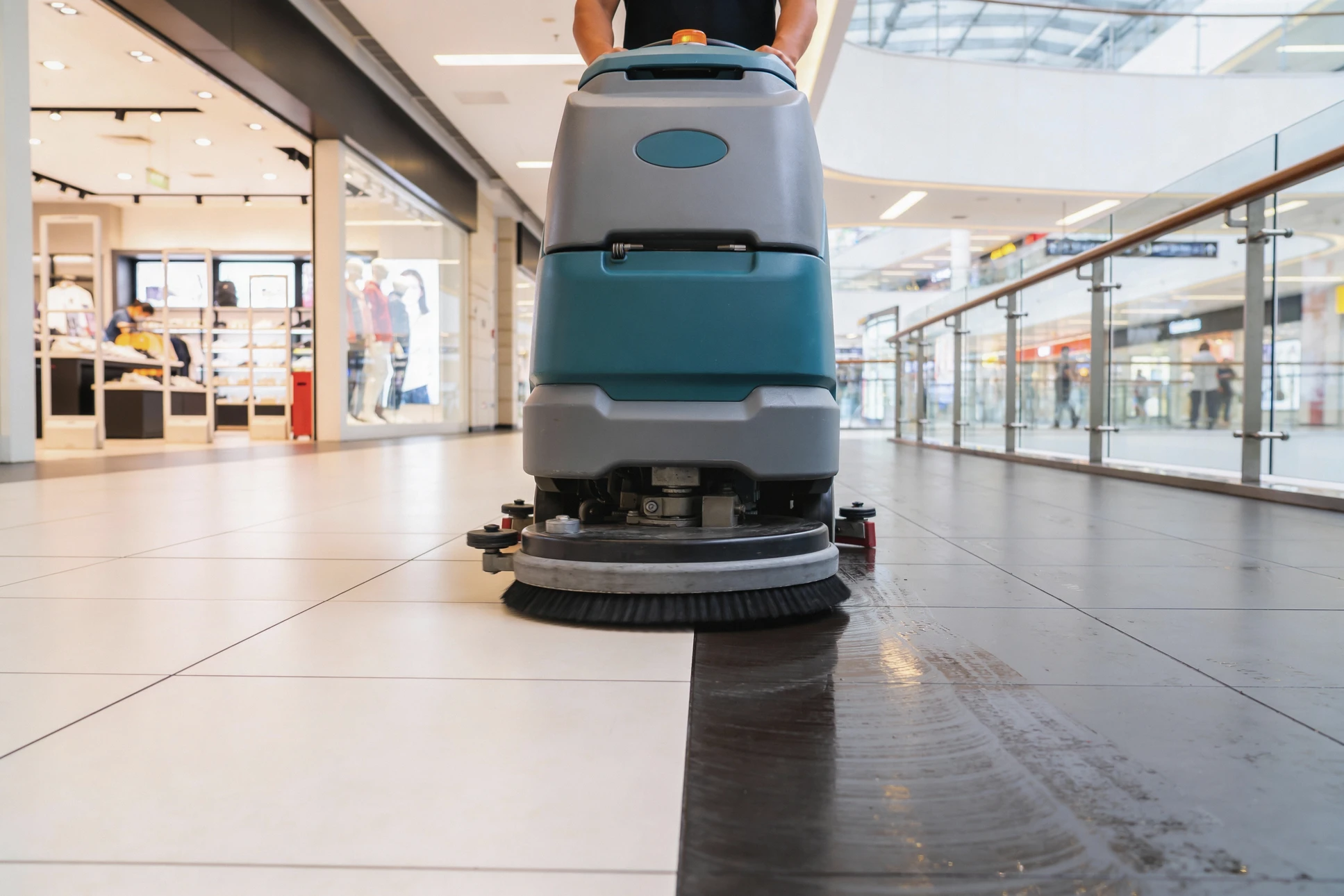 Intérieur de supermarché avec employé en combinaison bleue utilisant une autolaveuse professionnelle pour nettoyer le sol carrelé entre les rayonnages de produits alimentaires