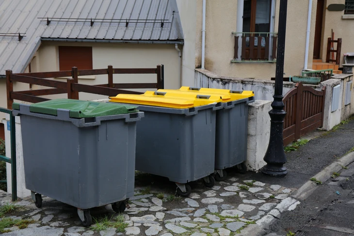 Benne à déchets orange remplie de sacs-poubelles bleus dans un environnement neutre